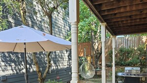A covered patio area with a table and chairs, a grill, and a large umbrella. - Charming Historic Grant Park Home / Atlanta Gem! (Atlanta)