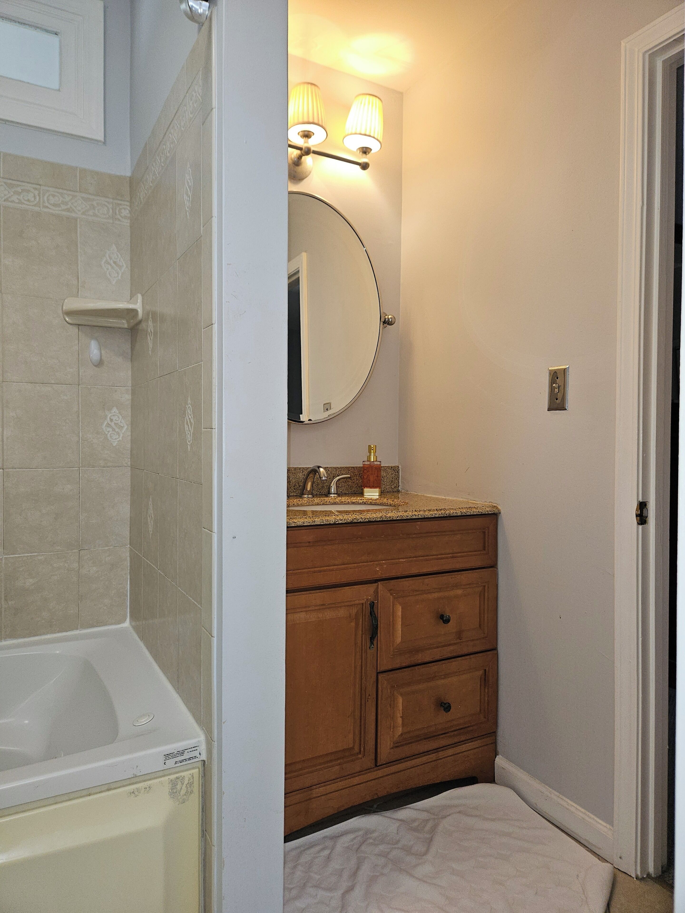 A bathroom with a bathtub, vanity with a mirror, and a towel on the floor.