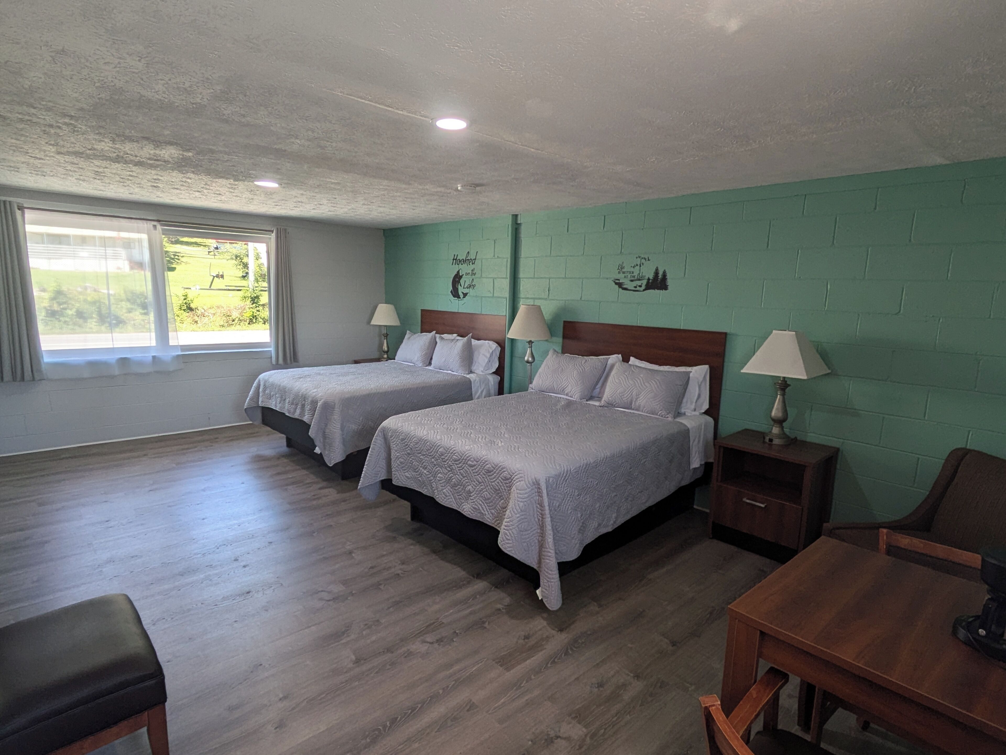 Una habitación con dos camas, un banco de madera, una mesa y una ventana con cortinas.