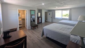 A hotel room with two beds, a desk, a chair, a small table, a TV, and a window with curtains.