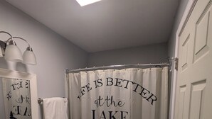 A bathroom with a shower curtain featuring a lake and paddle design, a white vanity with a mirror, and a towel hanging on the wall.