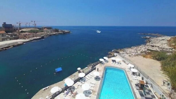 A coastal hotel with a swimming pool, a view of the sea, and a jet ski in the distance. - Lovely beachfront studio with pool-24h electricity & Family Duplex (Jabal Lubnan)