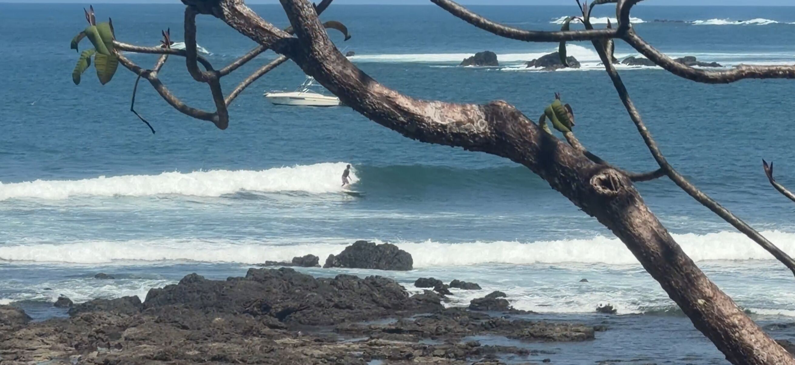A rocky shoreline with waves, a boat, and a person surfing.