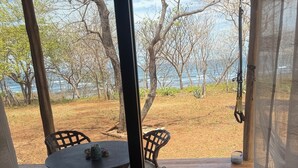 Un espacio al aire libre cubierto con una mesa y sillas, vista a la playa y un muelle de madera.
