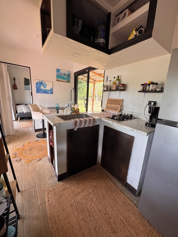 A compact kitchen with a central island, a dining area with a guitar, and a view of greenery outside.
