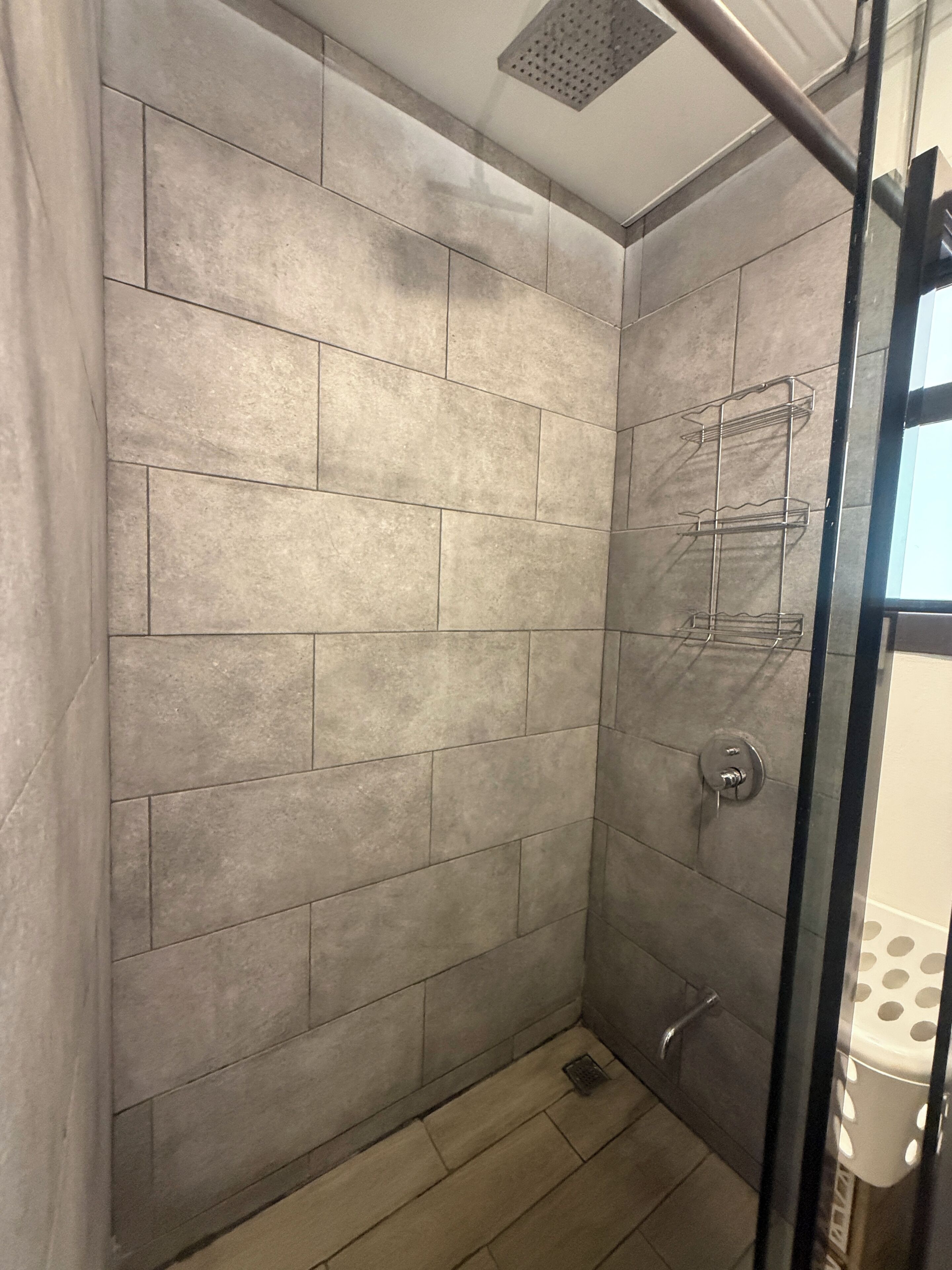 Eine Dusche mit gefliesten Wänden, einer Glastür und einem Metallregal.