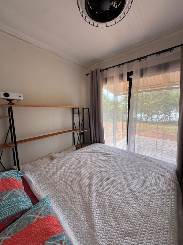 A bedroom with a bed, a ceiling fan, a projector, and a window with curtains.