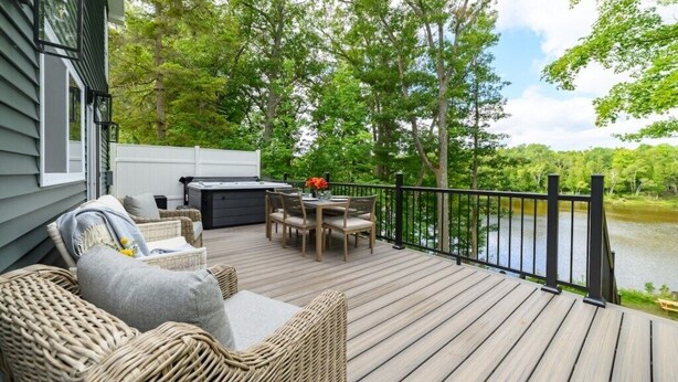 A deck with wicker furniture and a grill, overlooking a lake. - Newly Built|Riverfront|Kayaks|Hot tub|King|AC (Alpena)