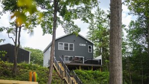 A two-story house with a deck, surrounded by trees and greenery. - Newly Built|Riverfront|Kayaks|Hot tub|King|AC (Alpena)