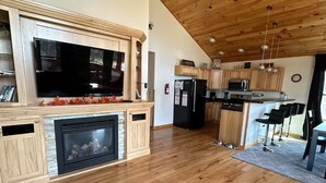 Eine geräumige Küche mit Holzboden, einem integrierten Fernseher, einem Kamin und modernen Geräten.