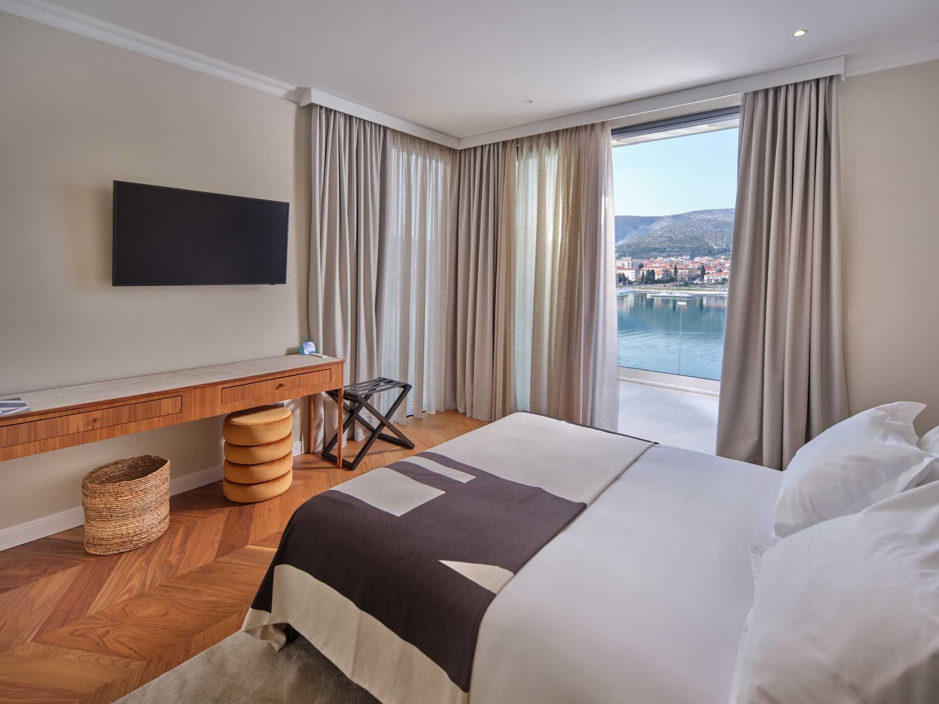 Une chambre d’hôtel équipée d’un lit, d’un bureau, d’une chaise, d’une télévision et offrant une vue sur un lac et des montagnes.