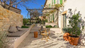 A courtyard with a stone wall, a wooden bench, a pergola, and a potted plant.