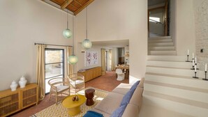A spacious living area with a high ceiling, a dining set, and a staircase.