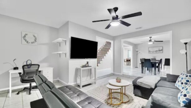 A modern living room with a grey sofa, a black bench, a white coffee table, and a TV mounted on the wall. - Large  House in Peaceful McAllen. Large Pool, 10th/Trenton. Perfect Location (McAllen)