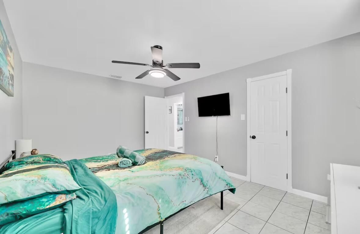 A bedroom with a bed, a ceiling fan, a TV mounted on the wall, and a door.