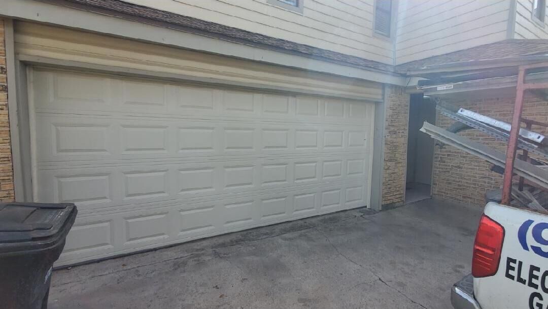 Een garage met een gesloten witte deur, een bakstenen muur en een ladder die tegen de muur staat.