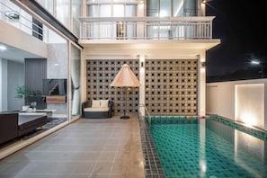 A modern indoor swimming pool with a tiled floor, a seating area with a sofa and a lamp, and a patterned wall in the background. - La Lune Pool Villa Chiang Mai (Saraphi)