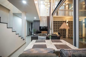 Un salon moderne avec un canapé, une table basse et un téléviseur. Un escalier mène à un niveau supérieur.
