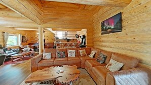 A log cabin interior with a large L-shaped leather sofa, a wooden coffee table, and a painting of a forest scene. - The Oak & The Log Cabin, Sleeps 10, 2 Hot Tubs (Oakenshaw)