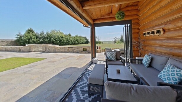 A wooden cabin with a patio area featuring a sofa, cushions, and a table. - The Oak & The Log Cabin, Sleeps 10, 2 Hot Tubs (Oakenshaw)