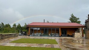 Uma cabana moderna de madeira com telhado vermelho, grandes janelas de vidro e um alpendre de pedra.