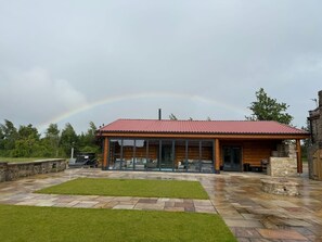 A modern wooden cabin with a red roof, large glass windows, and a stone patio. - The Barn & The Log Cabin, Sleeps 12, 2 Hot Tubs (Oakenshaw)
