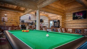 Interior acolhedor de uma cabana de registos, com mesa de bilhar, paredes de madeira e uma televisão.