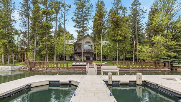 A house with a dock leading to a pond, surrounded by tall trees.
