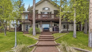 A two-story house with a balcony, a stone fireplace, and a wooden deck leading to the entrance.