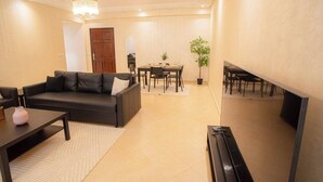 A living room with a sofa, coffee table, and TV stand. There is a dining area with a table and chairs.
