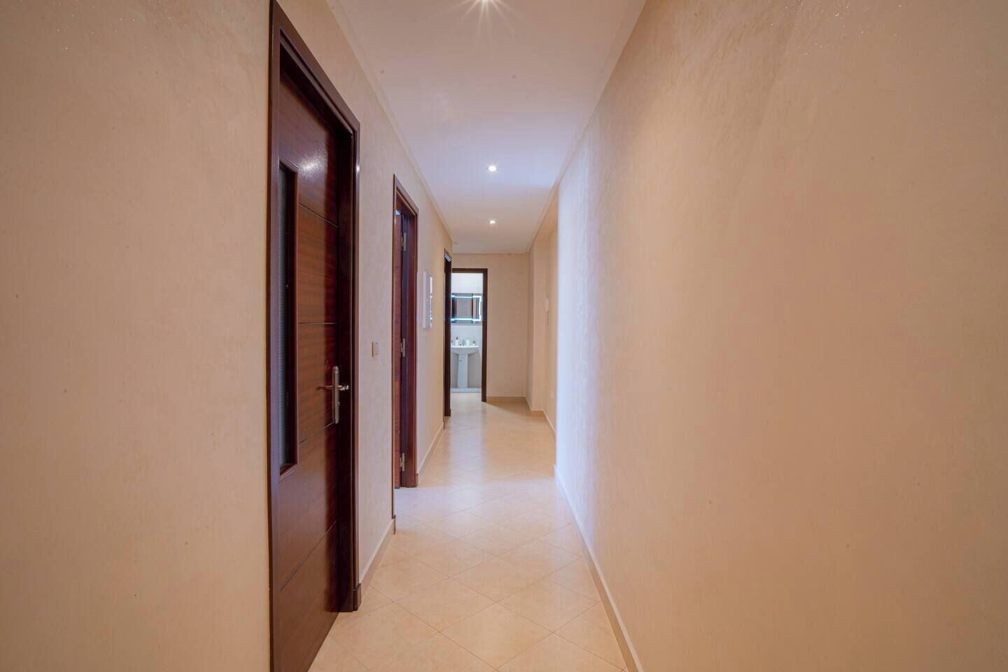 A narrow hallway with wooden doors and a light-colored tiled floor.