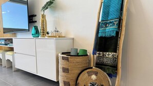 A modern room with a white cabinet, a large mirror, a plant, and a woven basket with a kettle.