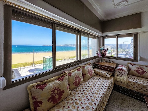 A room with a large window overlooking a beach and cityscape.