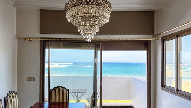 A room with a dining table and chairs, a chandelier, and a view of the ocean through a sliding glass door. - Stunning 3-bedroom apartment  with panoramic ocean views, located in the heart of Tangier´s playa (Tangier)