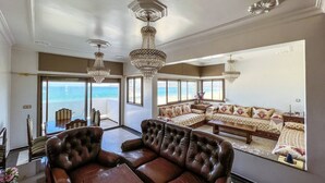 A spacious living room with a large leather sofa, a wooden coffee table, and multiple windows offering a view of the sea. - Stunning 3-bedroom apartment  with panoramic ocean views, located in the heart of Tangier´s playa (Tangier)