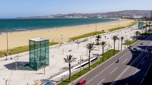 A coastal cityscape with a beach, a modern glass building, and a road with vehicles. - Stunning 3-bedroom apartment  with panoramic ocean views, located in the heart of Tangier´s playa (Tangier)
