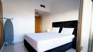 A bedroom with a large bed, a wooden door, and a wall-mounted ironing board. - The perfect coastal getaway, just steps from the beach, with a private balcony, open living area. (Tangier)