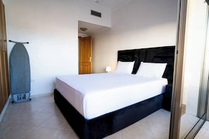 A bedroom with a large bed, a wooden door, and a wall-mounted ironing board.