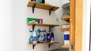 A laundry area with a front-loading washing machine, shelves with cleaning supplies, and a ceiling fan. - The perfect coastal getaway, just steps from the beach, with a private balcony, open living area. (Tangier)