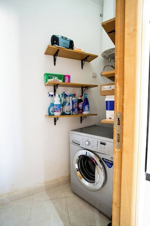 A laundry area with a front-loading washing machine, shelves with cleaning supplies, and a ceiling fan.