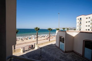 A balcony with a view of a beach, palm trees, and a clear blue sky.