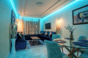 Una sala de estar moderna con una mesa de comedor de vidrio, sofá azul y plantas decorativas.
