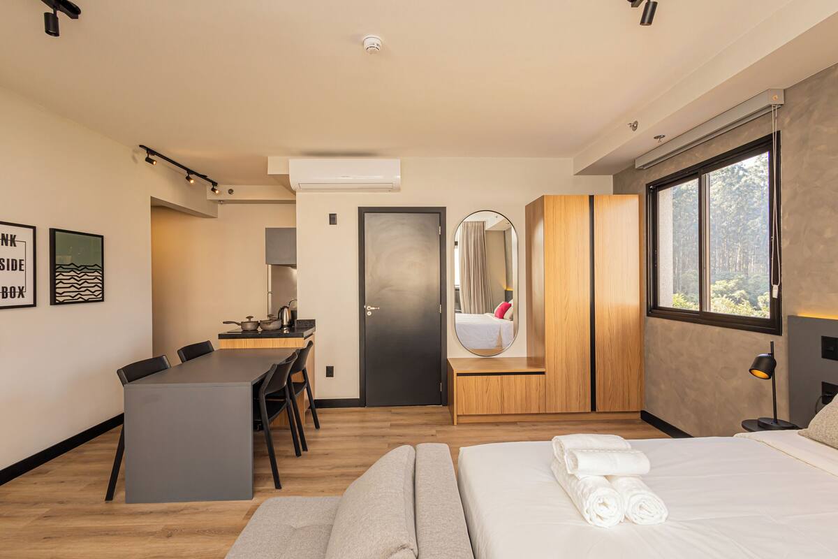 Une chambre d’hôtel moderne équipée d’un lit, d’un bureau, d’une chaise, d’une armoire et d’une grande fenêtre.