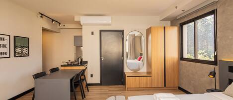 Una habitación de hotel moderna con cama, escritorio, zona de comedor y un ventanal grande.
