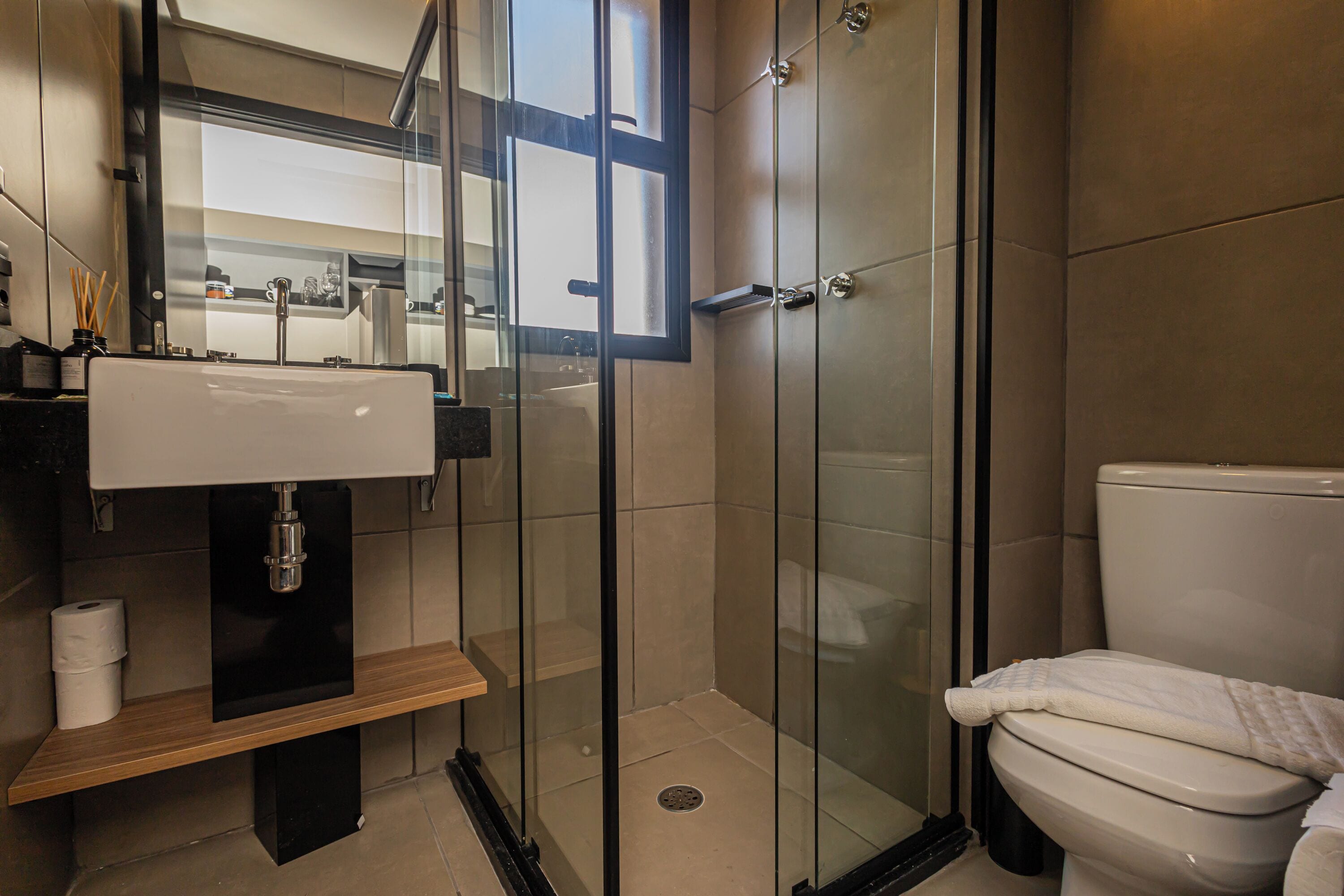 Een moderne badkamer met een douchecabine van glas, een wastafel met een houten plankje, en een toilet.