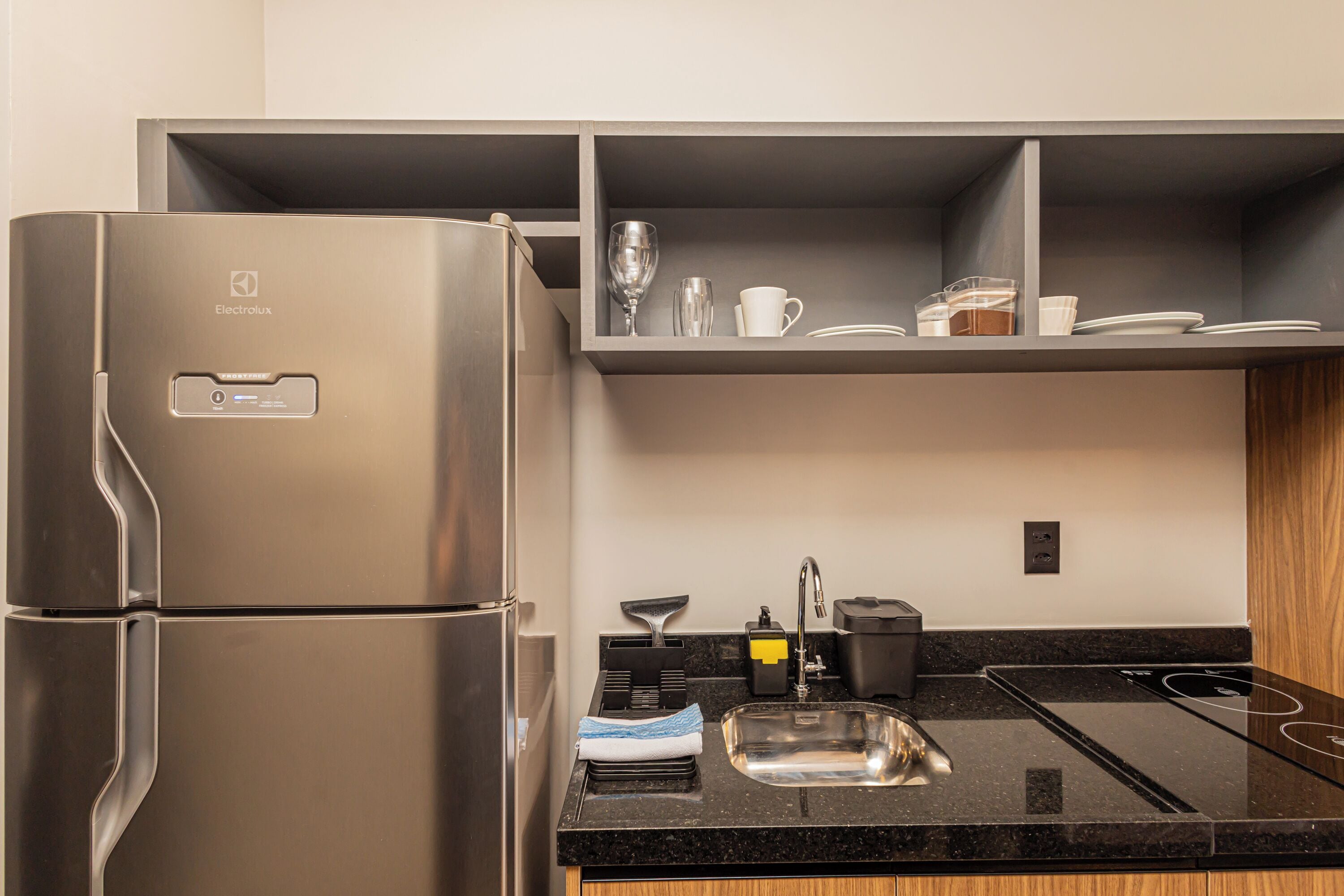 A modern kitchen with a stainless steel refrigerator, a black countertop, a sink, and a built-in oven.