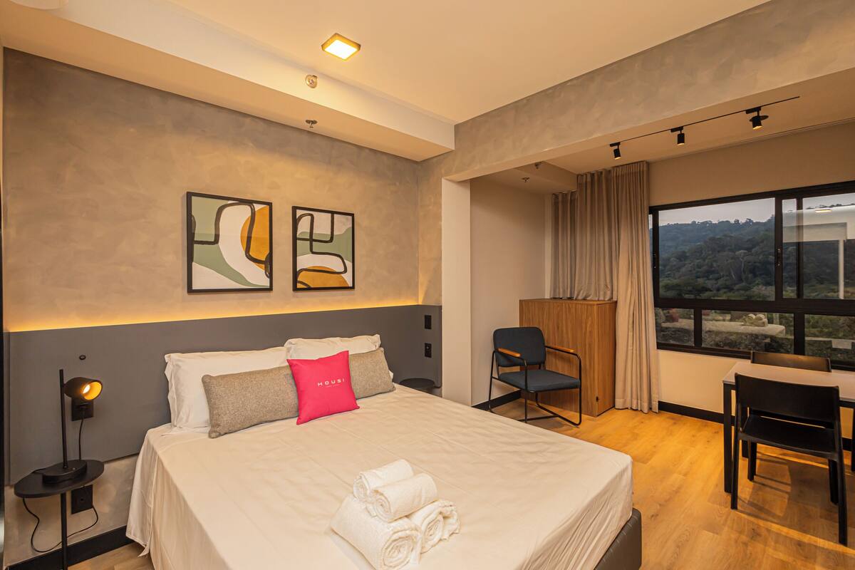 Une chambre d’hôtel moderne, dotée d’un grand lit, d’un bureau et offrant une vue sur l’extérieur.