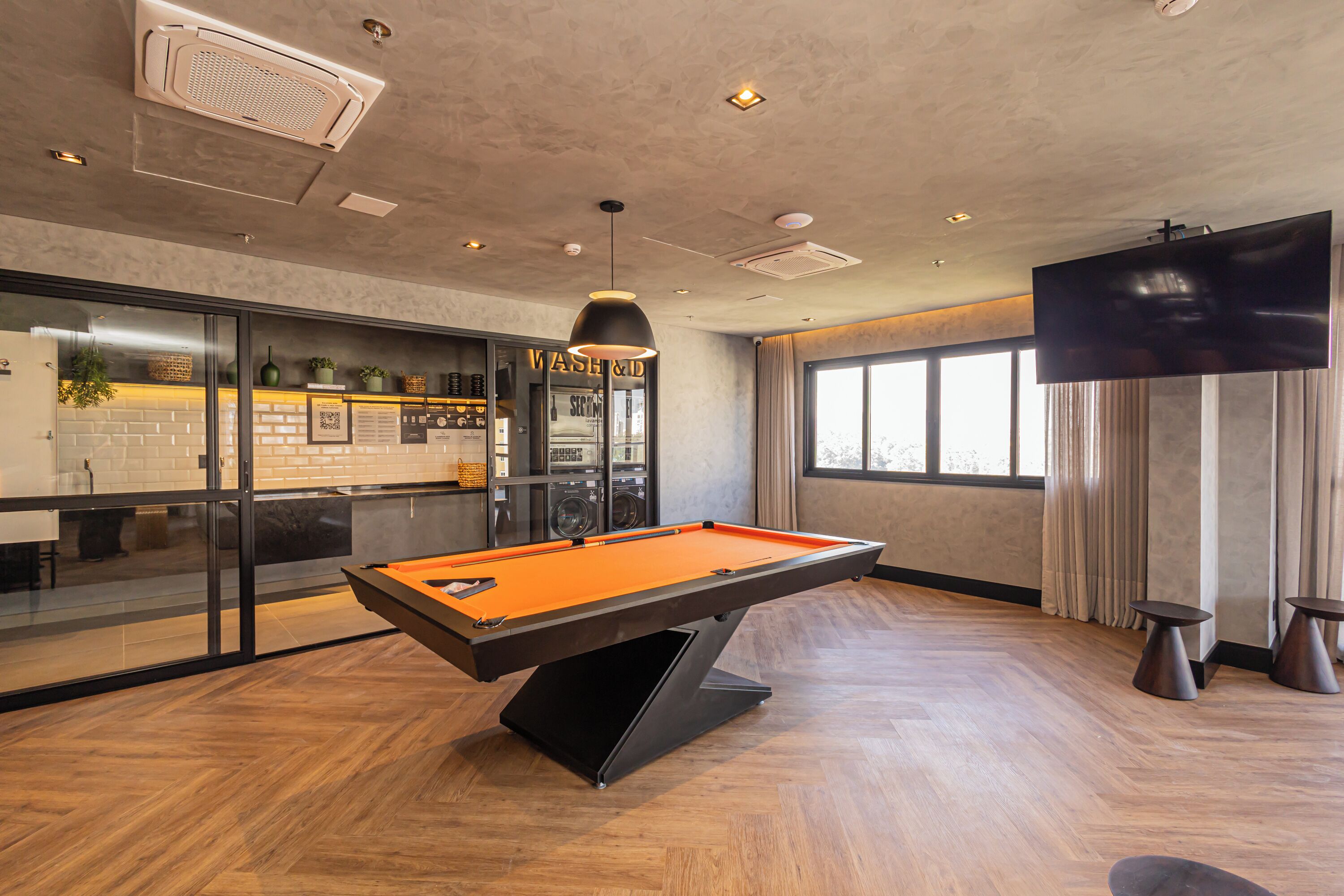 A pool table in a modern room with a bar area, a large TV, and a view of the outdoors.