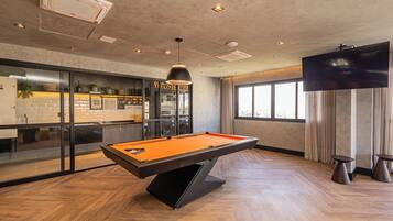 A pool table in a modern room with a bar area, a large TV, and a view of the outdoors.