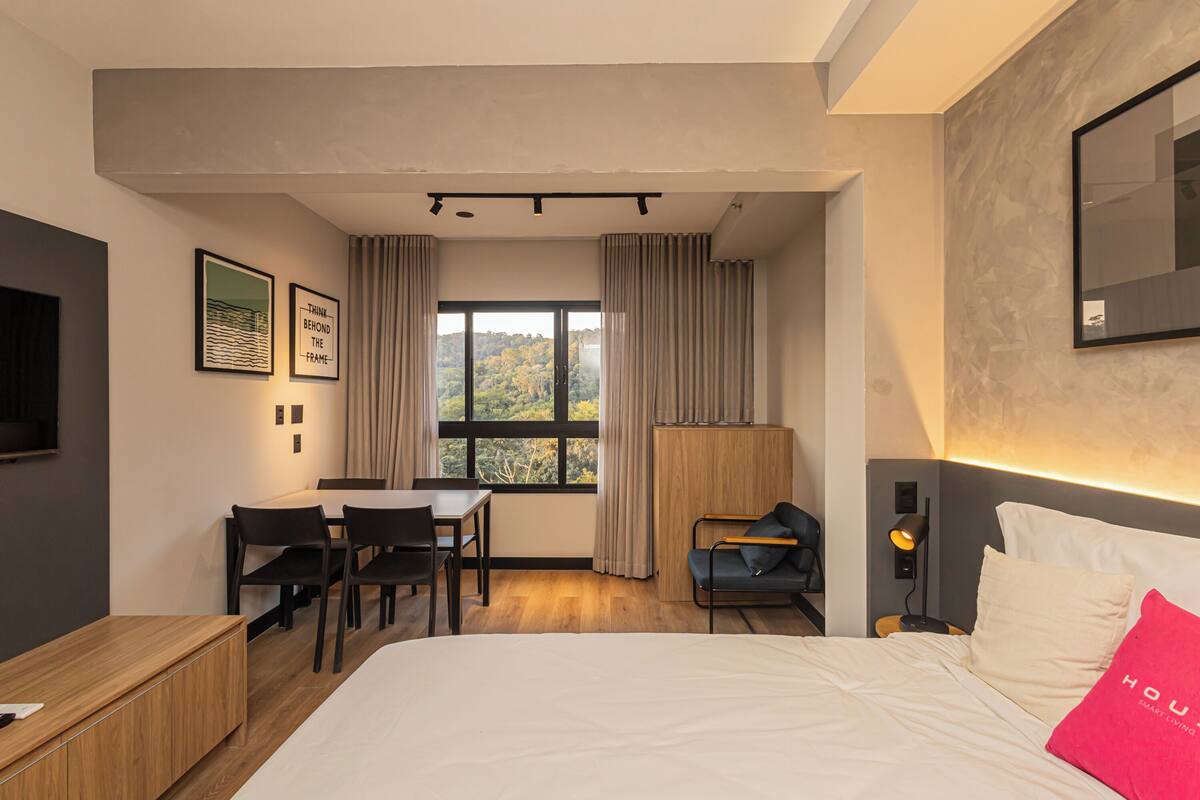 Une chambre d’hôtel moderne équipée d’un lit, d’un bureau, de chaises, d’une fenêtre avec des rideaux et d’un téléviseur fixé au mur.